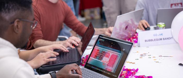 Four men sit at a round table playing videogames on laptops